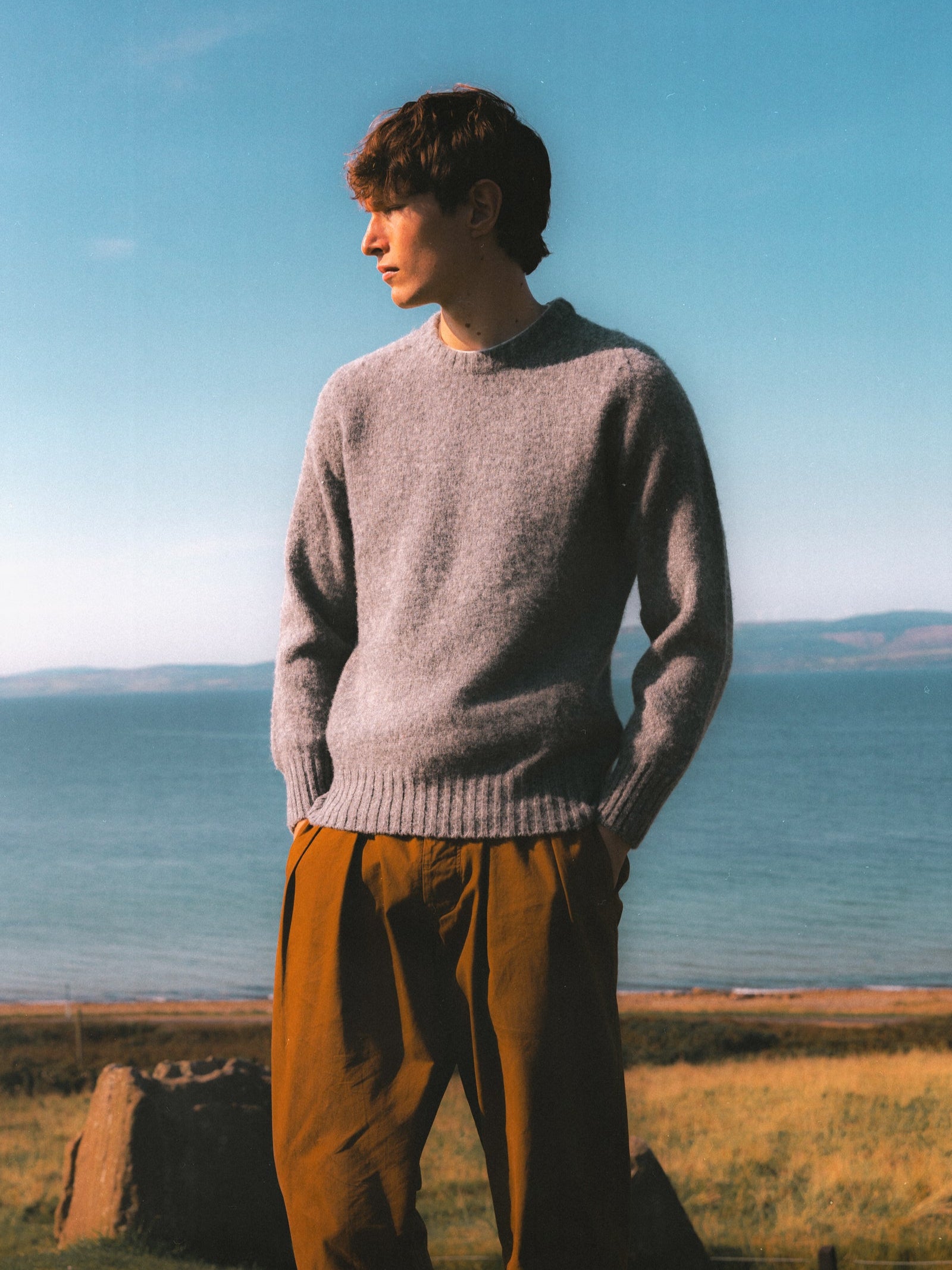 A model wearing a Made In Scotland knitted sweater in grey.