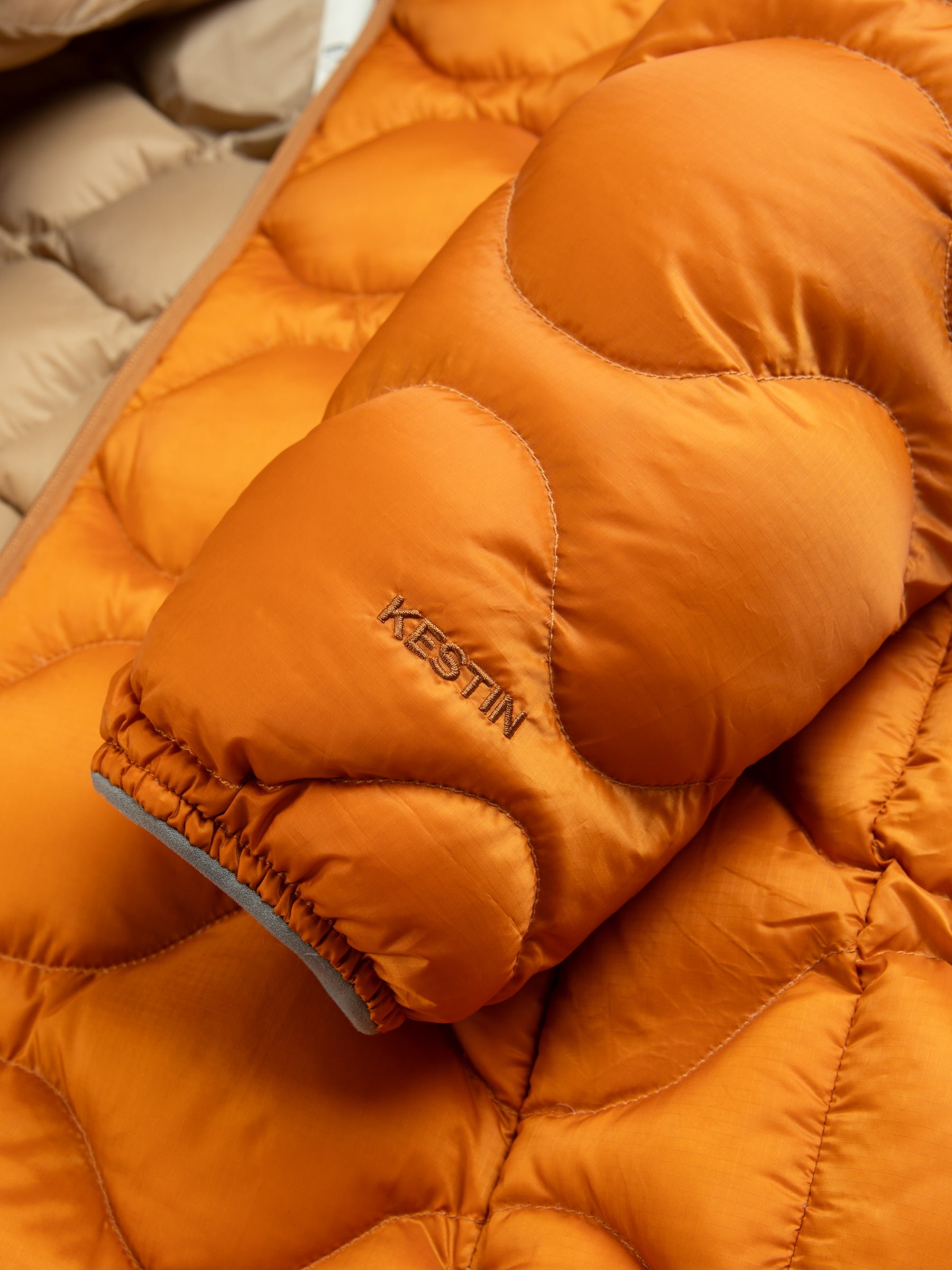The cuff of a men's technical down jacket with an embroidered logo in a bright orange colour.