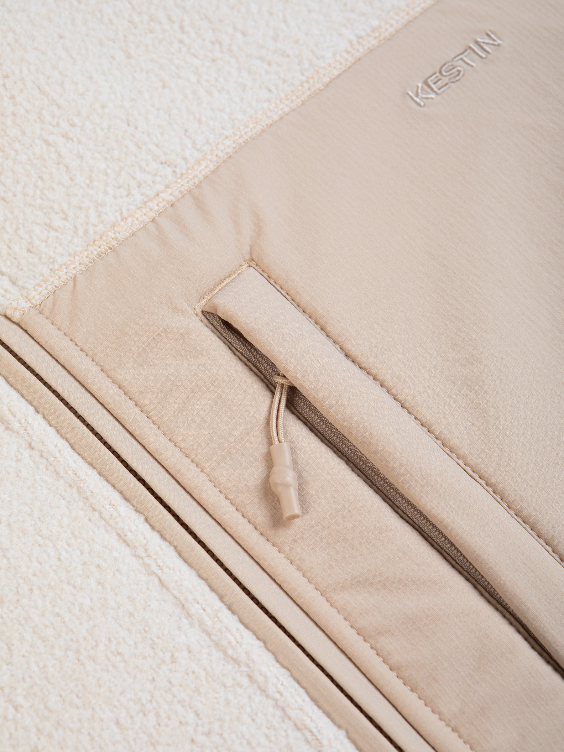 A men's fleece jacket material in an ecru white with a zippered pocket.