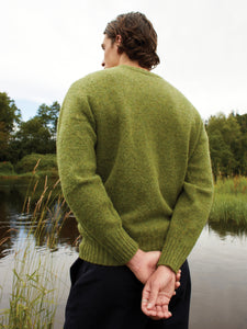A man wearing a green knitted sweater, made in Scotland from brushed Shetland wool.
