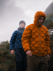 Two men hiking, wearing orange and navy down jackets in the rain.