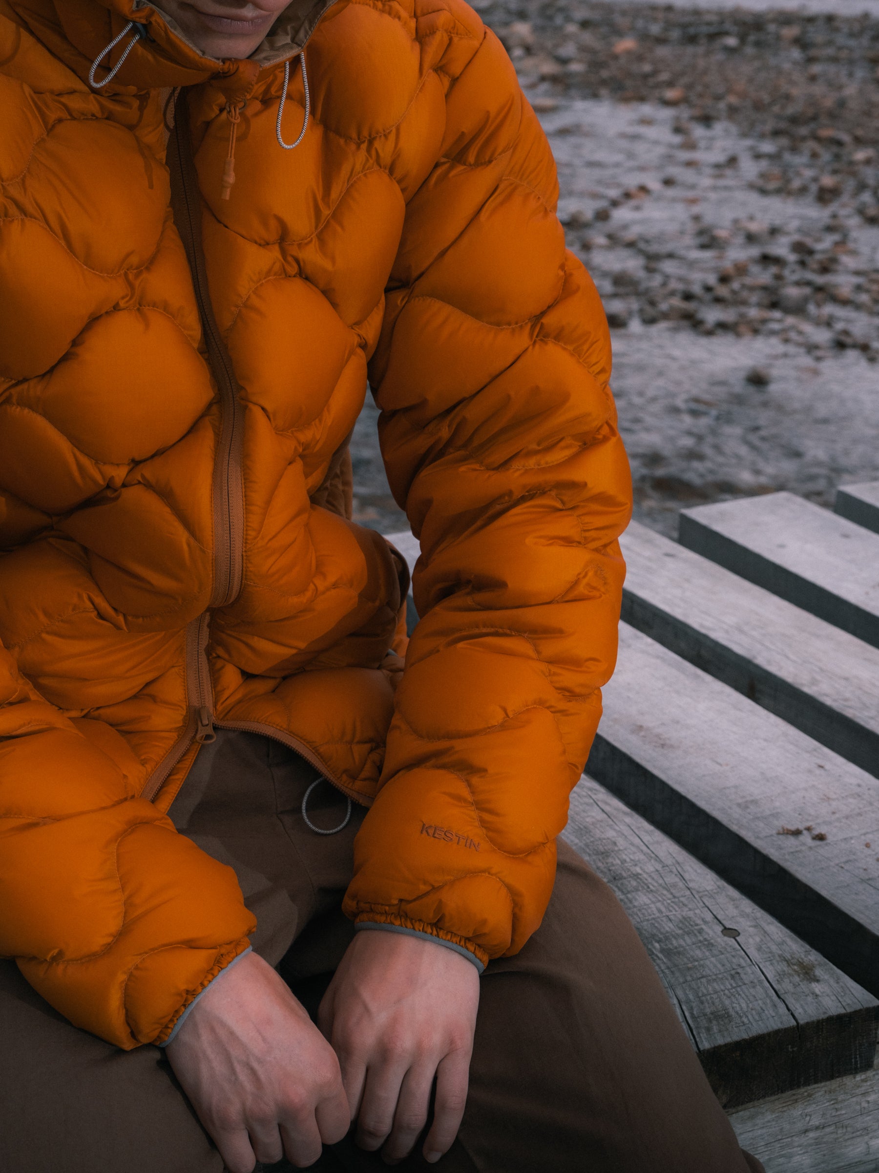 A man sitting on a bridge wearing a technical outdoor down jacket in orange.