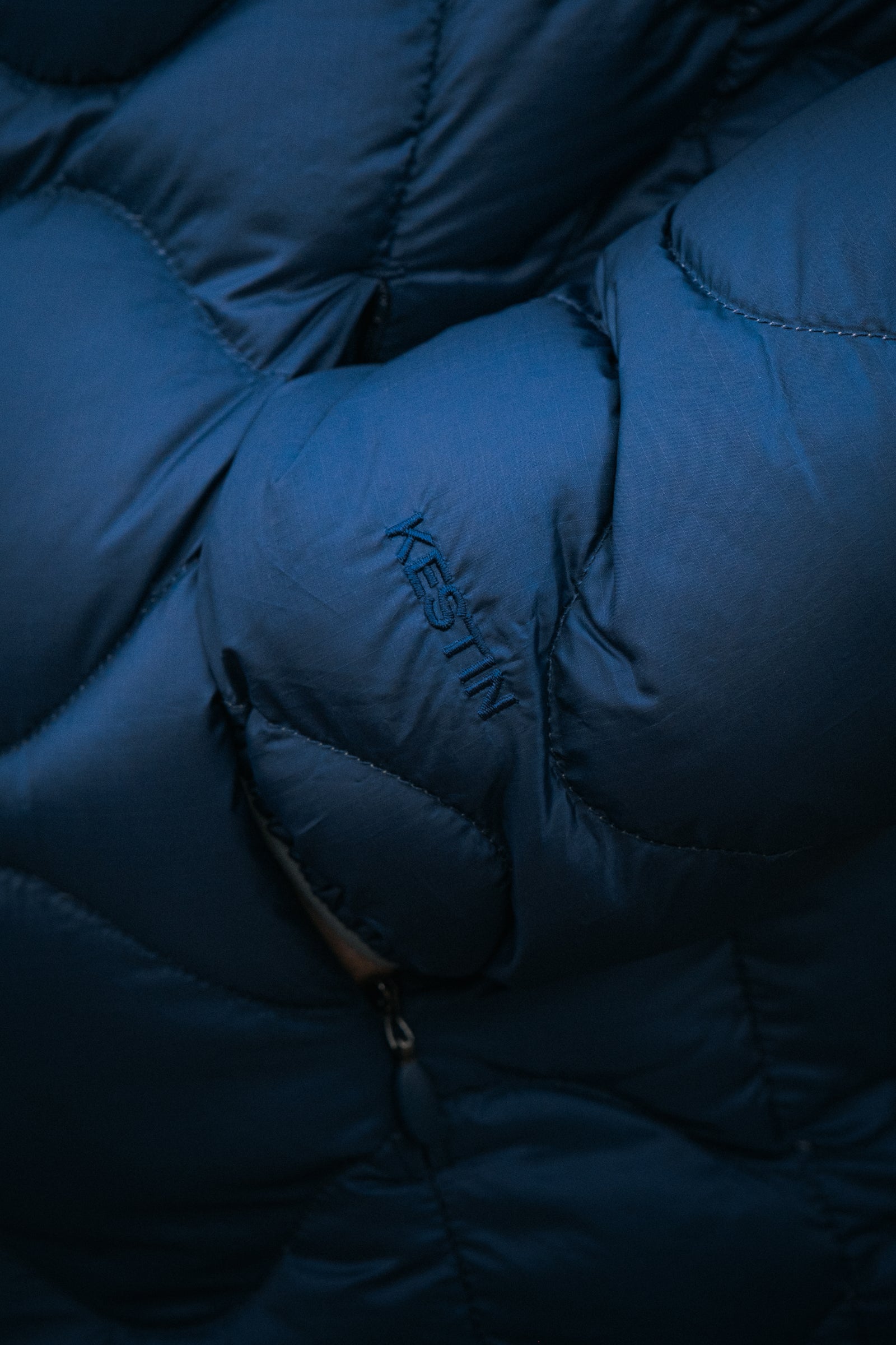 A hand in the pocket of the KESTIN Cuillin Down Jacket in Petrol Blue.