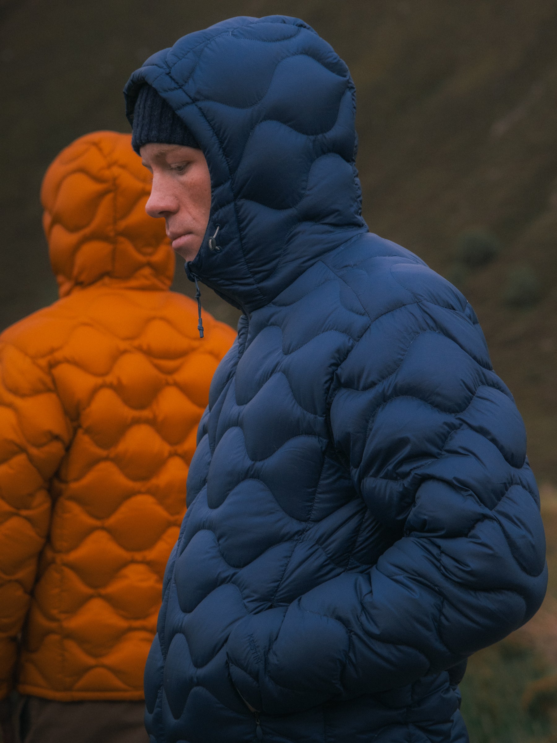 Two men on a mountain wearing blue and orange down insulated jackets.