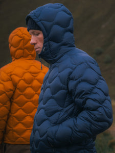Two men on a mountain wearing blue and orange down insulated jackets.