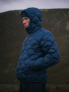 A man wearing an insulated down jacket in blue whilst standing on a mountain.