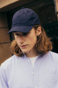 This man is wearing the Raeburn Button Down Shirt by KESTIN, which is made from a traditional Oxford Shirt material in Light Blue, with a Navy Blue baseball cap.