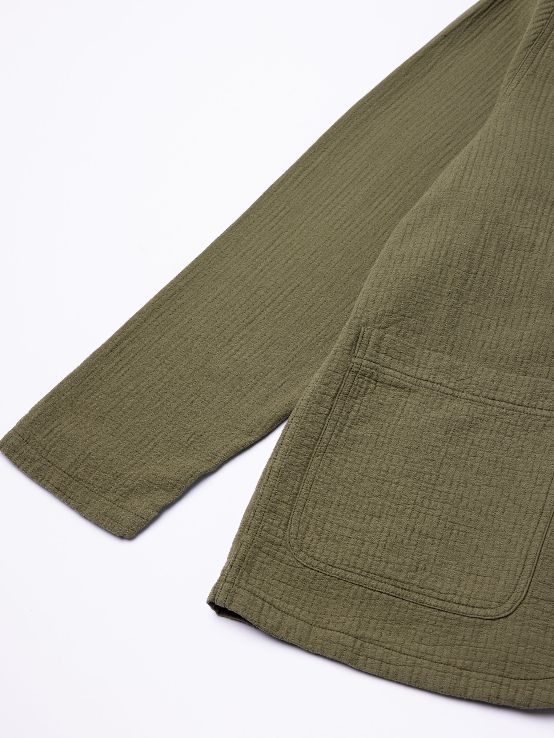 The hem and sleeve of an olive green chore coat from menswear brand KESTIN.