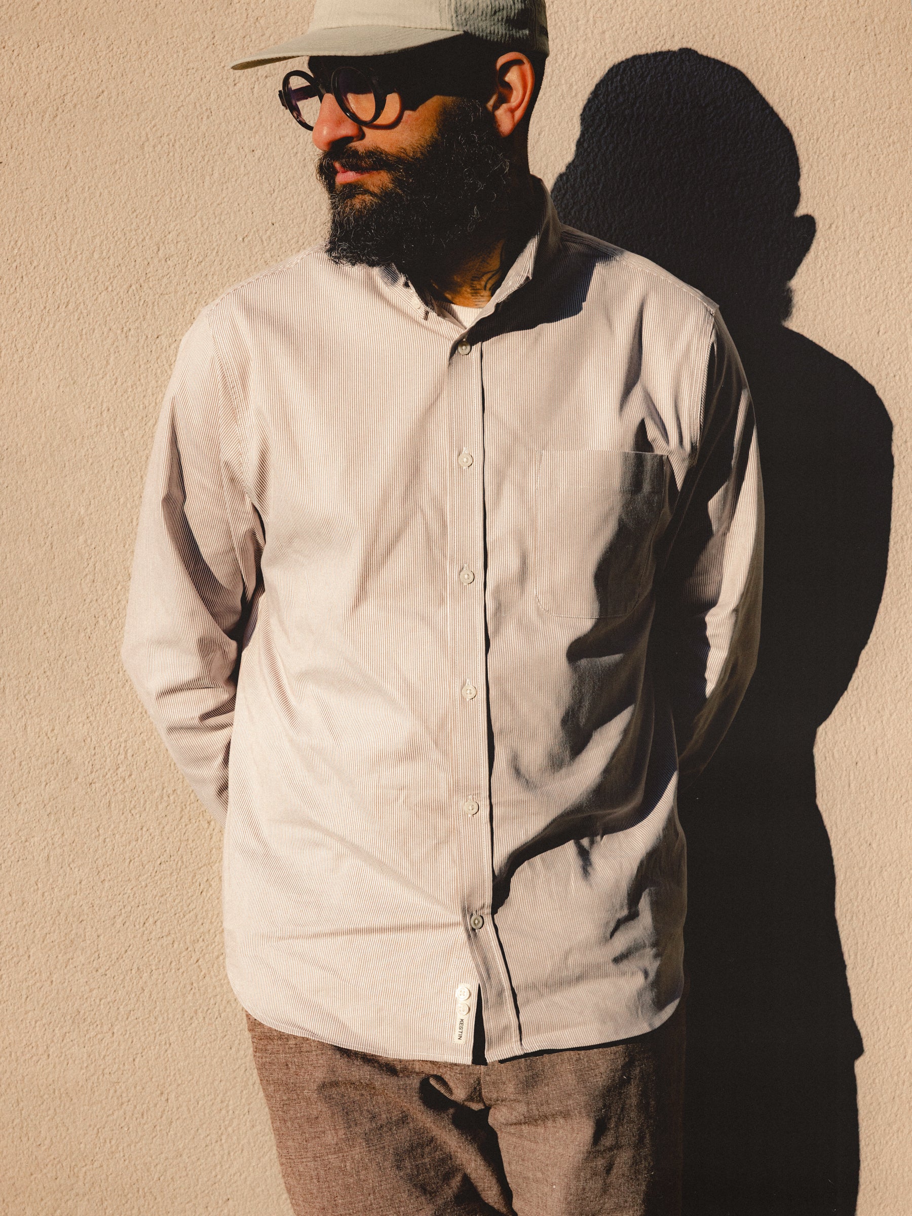 A model wearing a stripe shirt, trousers and a cap from menswear brand KESTIN.
