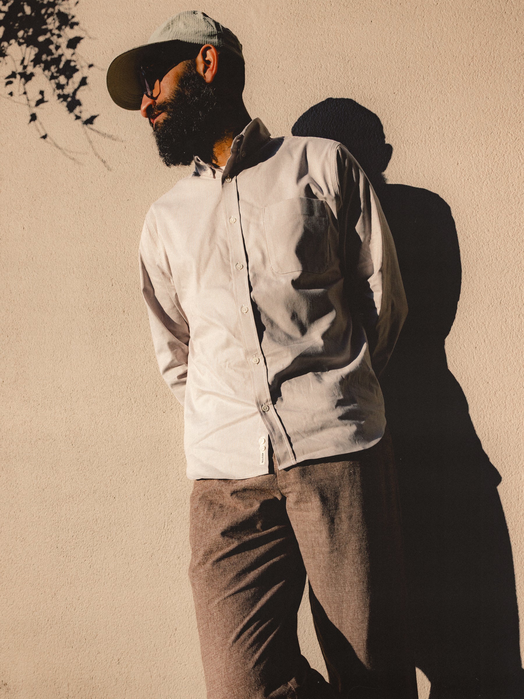 A man leaning against a wall, wearing clothing from Scottish menswear brand KESTIN.