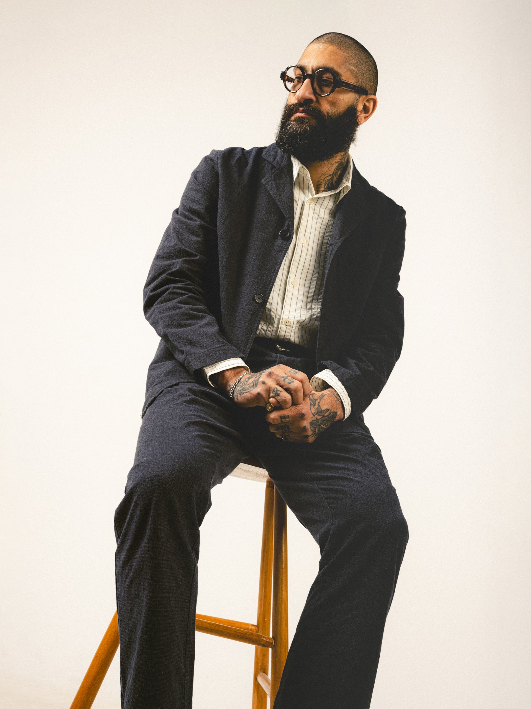 A man leaning on a stool, wearing a charcoal grey suit from Scottish brand KESTIN.