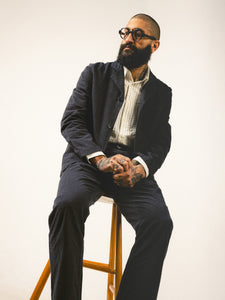 A man leaning on a stool, wearing a charcoal grey suit from Scottish brand KESTIN.