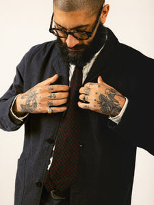 A man with glasses and traditional hand tattoos fixing the fit of his charcoal grey suit.