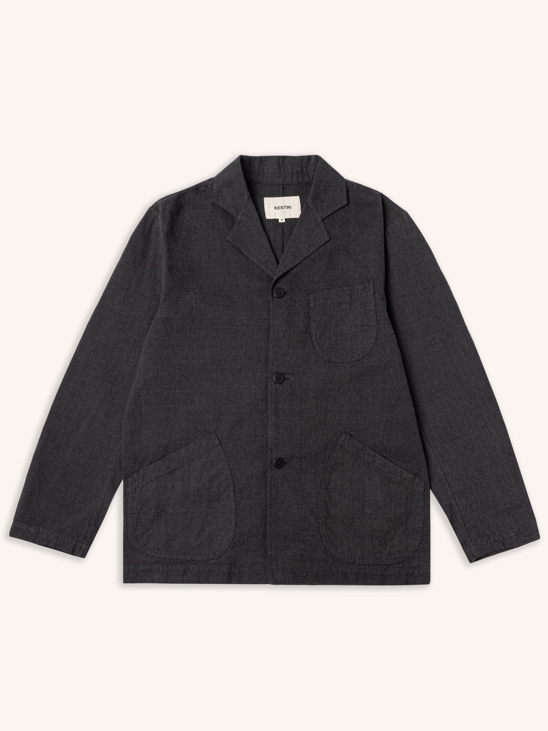 A men's blazer which has taken details from a chore coat, in charcoal grey, and on a white background.