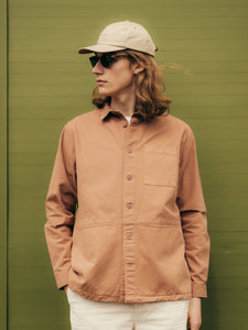 A model wearing a cotton twill cap by KESTIN, alongside a long sleeve overshirt.