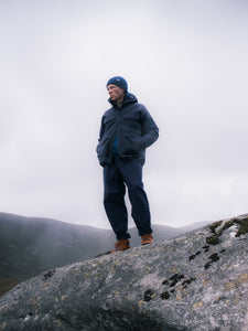 A man standing on a mountain in the mist, wearing a navy blue waterproof jacket.