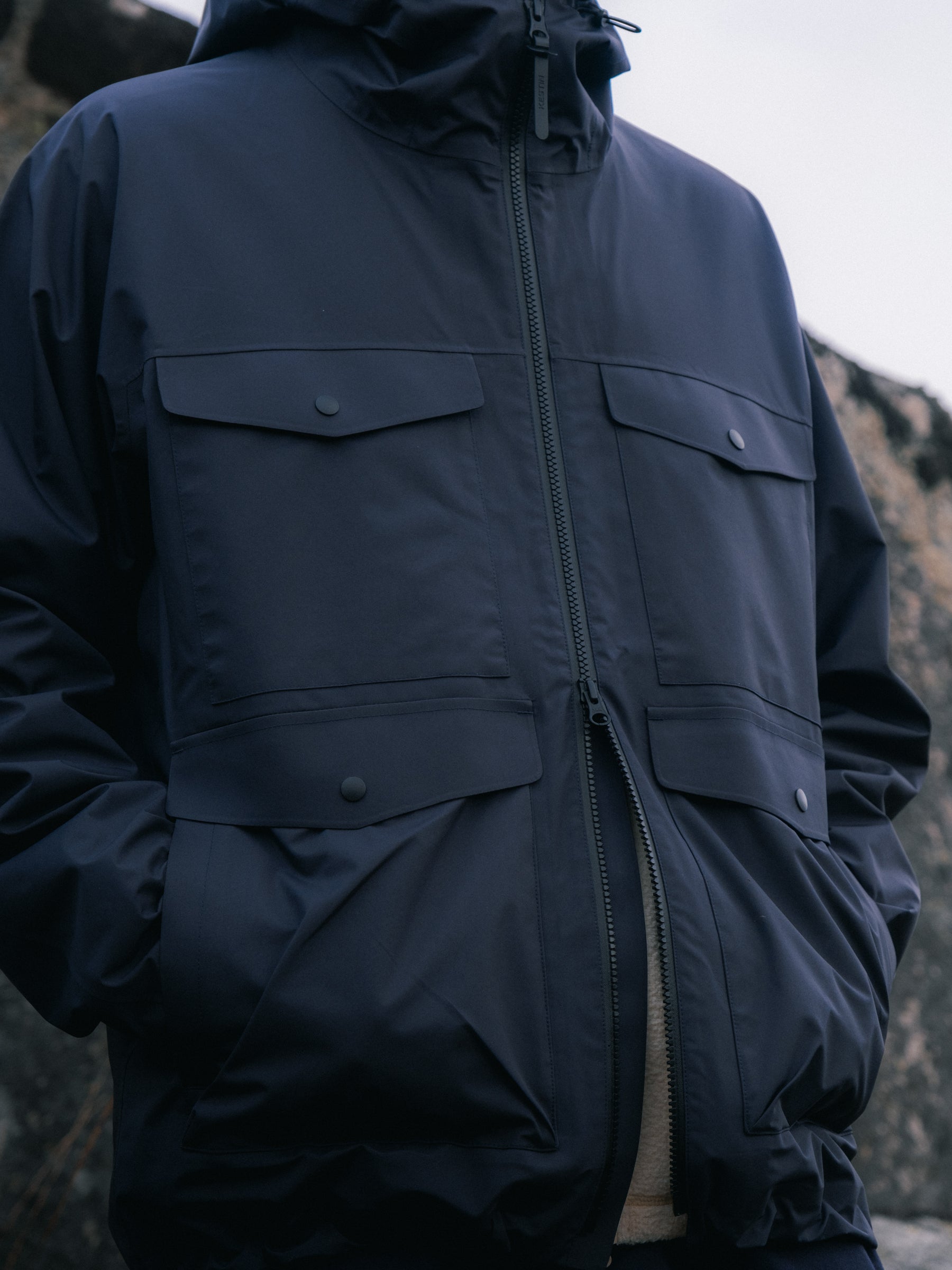 A man wearing a navy blue waterproof jacket with his hands in his pockets.