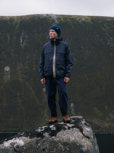 A man standing in the mountains wearing a navy blue waterproof shell jacket.