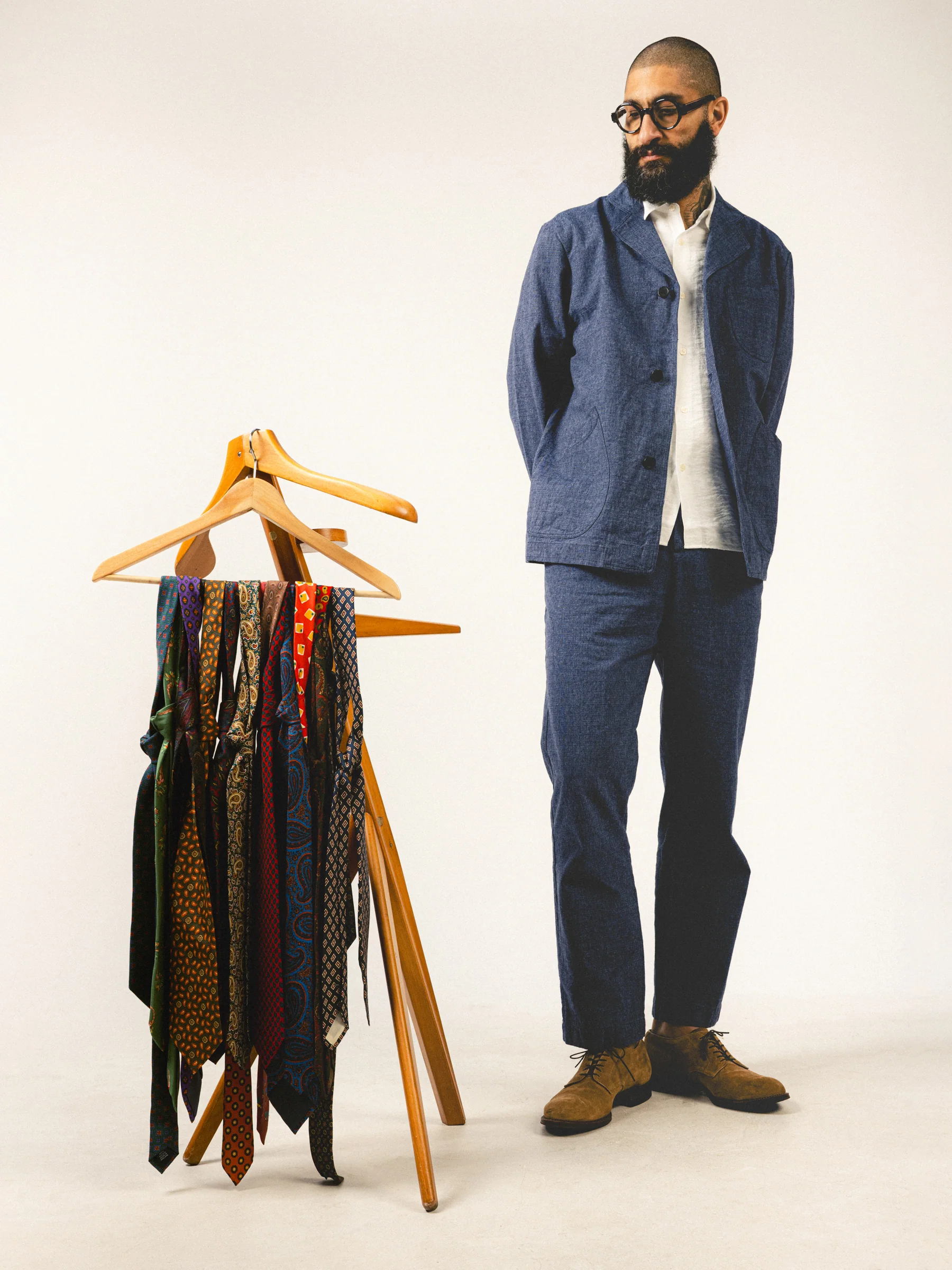 A model wearing an indigo blue suit from Scottish menswear brand KESTIN, stood next to a collection of ties.