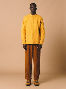 A bright autumnal outfit, with a model wearing a yellow shirt and brown trousers from KESTIN.