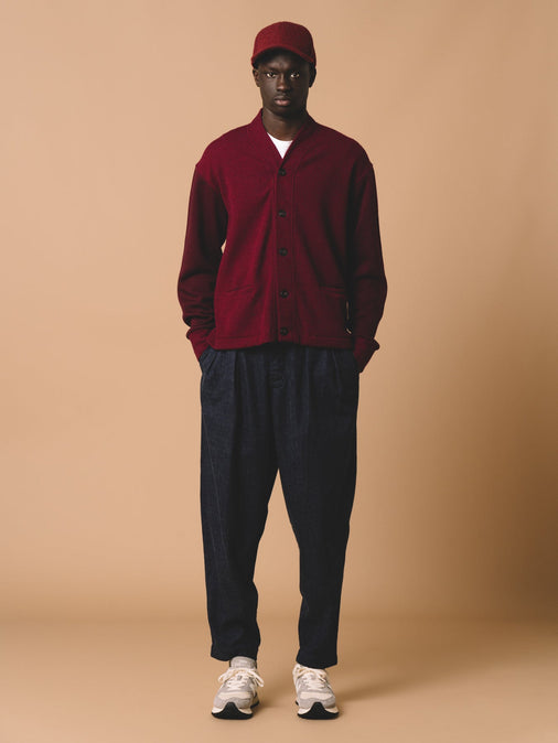 A model wearing a knitted wool cardigan in dark red, with indigo denim trousers.