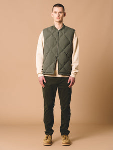 A model wearing a layered autumn/fall outfit, with green trousers and an insulated gilet.