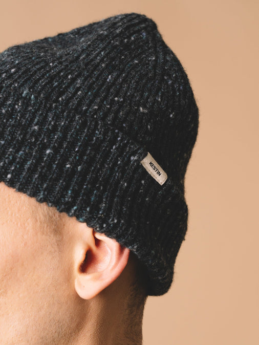 A woven logo tag, sewn to a knitted beanie, made in Scotland from wool.