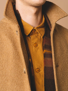 A man wearing a knitted wool scarf and a designer wool overcoat, over a simple workwear shirt.