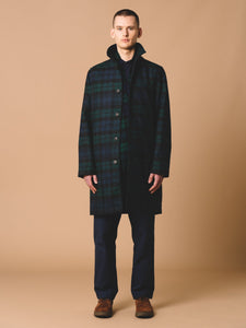 This man is wearing an Edinburgh Overcoat from the Autumn/Winter 2023 collection by Scottish designer KESTIN, in a traditional Black Watch Tartan check. He's wearing it with the collar turned up.