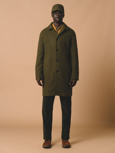 A man wearing a dark green overcoat, designed for winter and made from a warm Italian wool, designed by British menswear designer KESTIN.