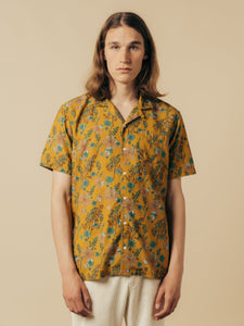 A model wearing a short sleeve shirt in a yellow floral graphic print.