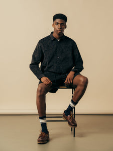 A model sitting on a stool, wearing blue paisley clothing from premium menswear brand KESTIN.