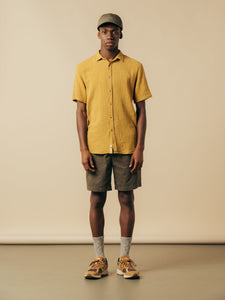 A model wearing a yellow short sleeve shirt with olive green shorts.