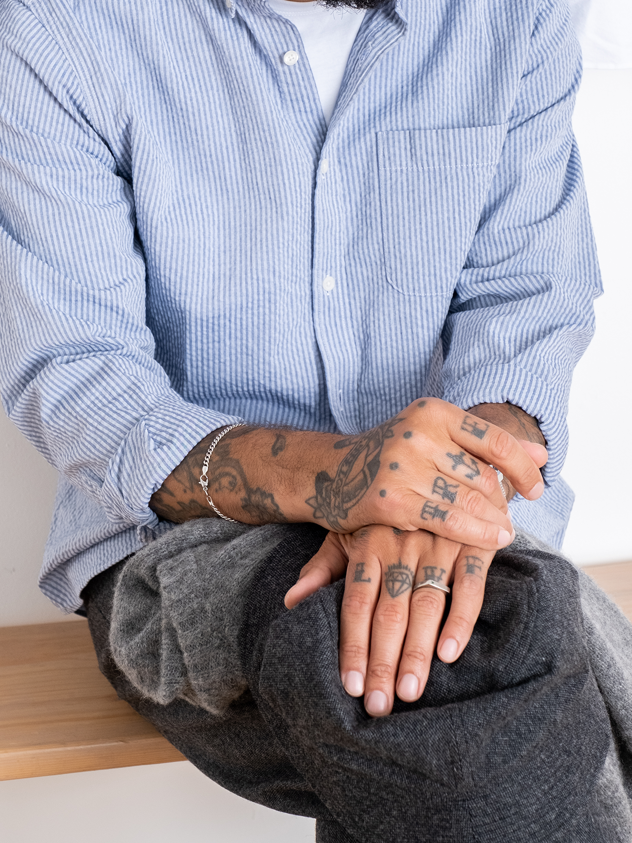 A man wearing the Raeburn Shirt by designer brand KESTIN, made from a striped Seersucker material, with the sleeves rolled up to show traditional arm and hand tattoos.