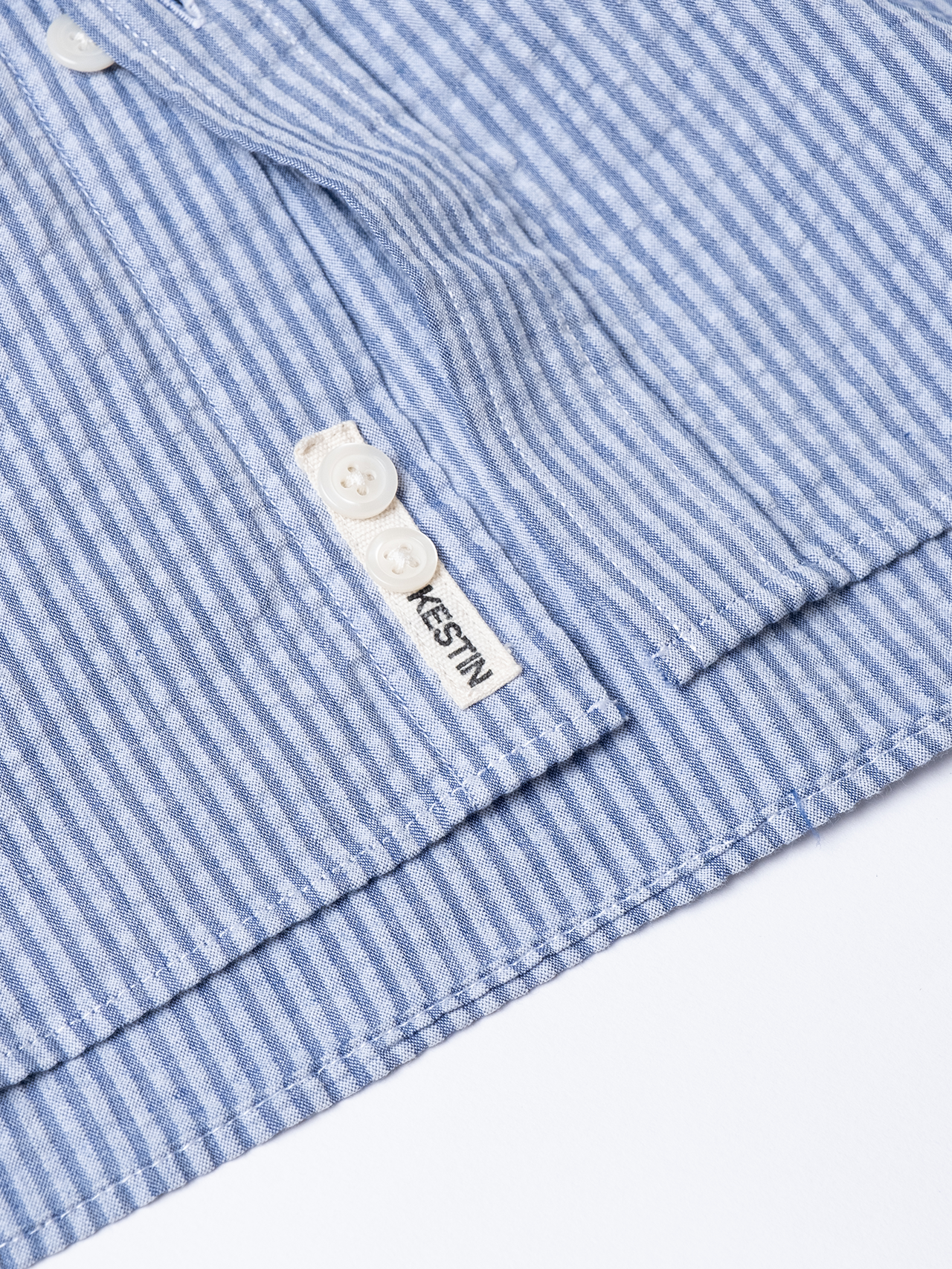 A woven logo patch, sewn to the front of a long sleeve men's shirt by British designer clothing brand KESTIN.